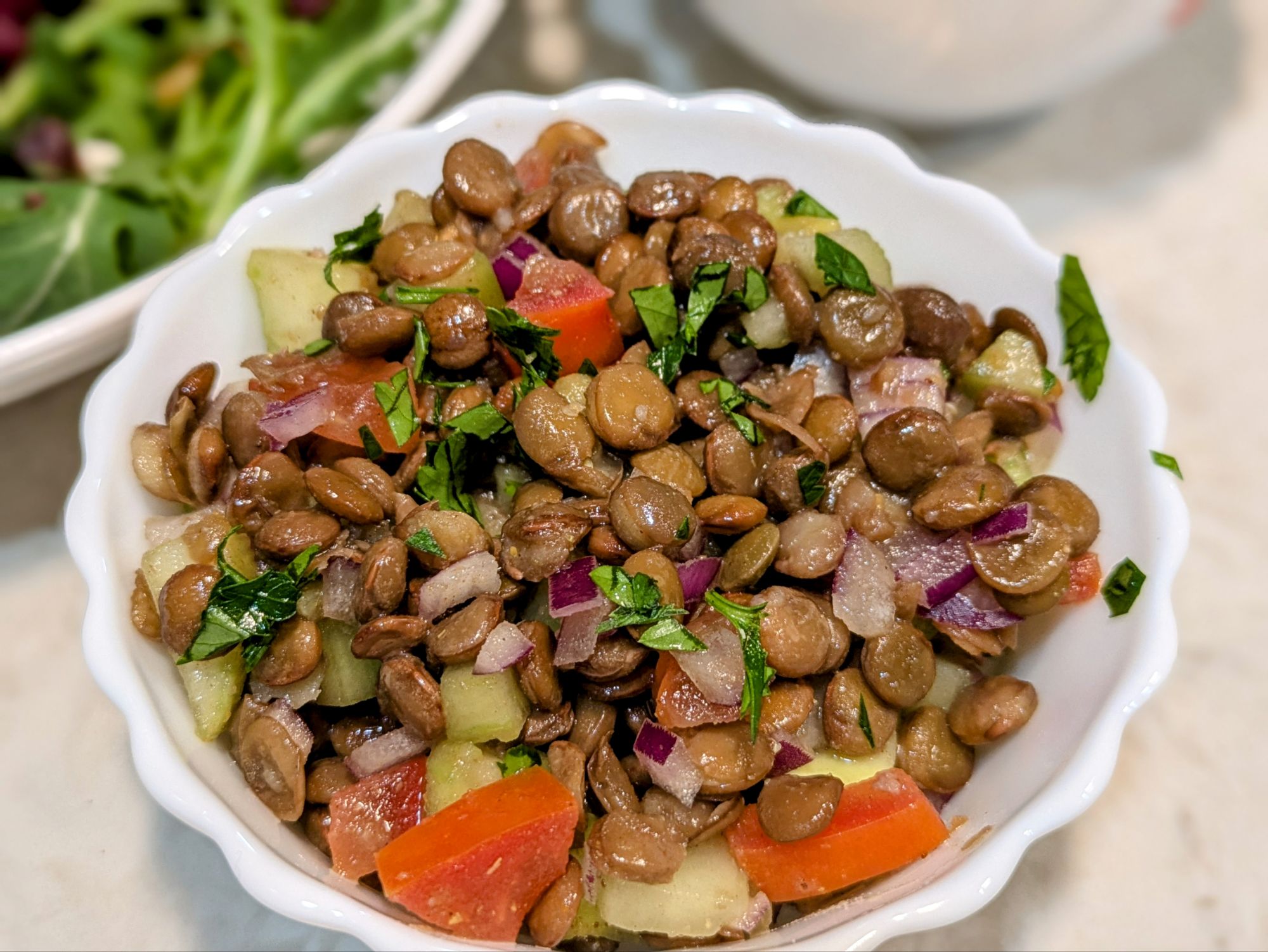 A vibrant green lentil salad bursting with color, featuring tender lentils mixed with diced tomatoes, chopped scallions, fresh parsley, and mint. Drizzled with olive oil and sprinkled with red chili flakes, it’s inviting you to dig in